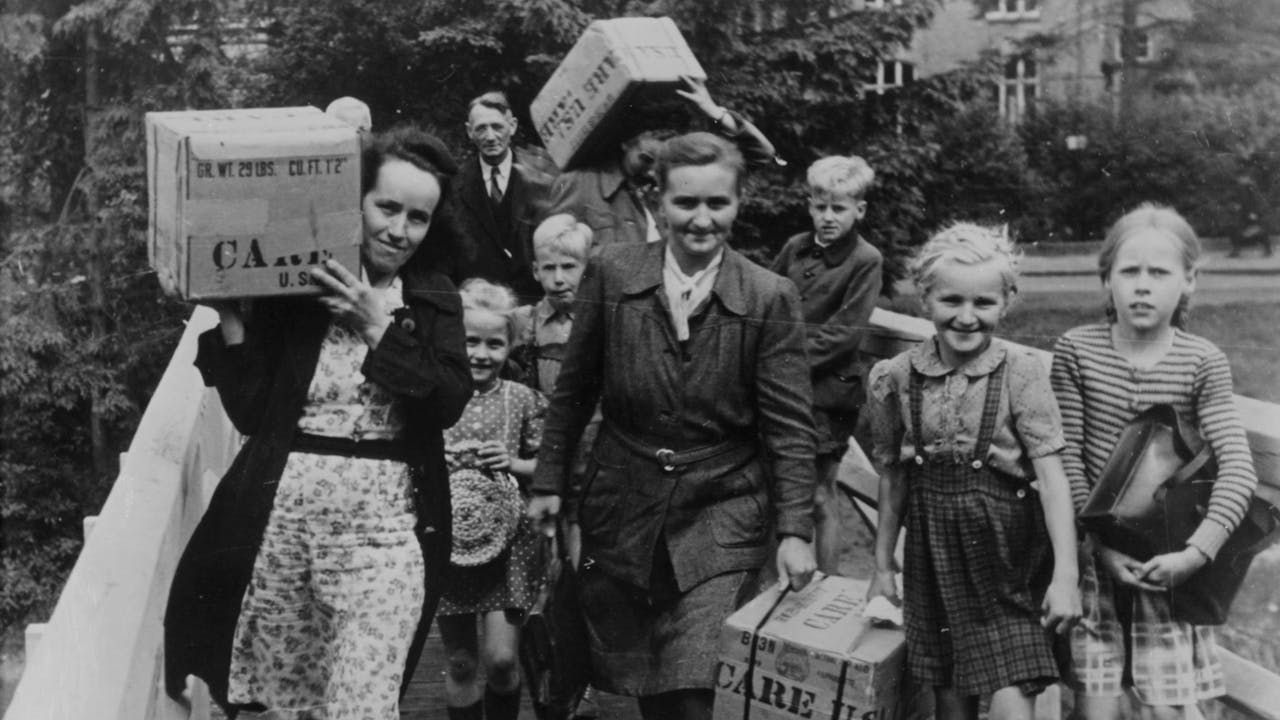 Historische zwart-witfoto: een groep mensen draagt een CARE-pakket