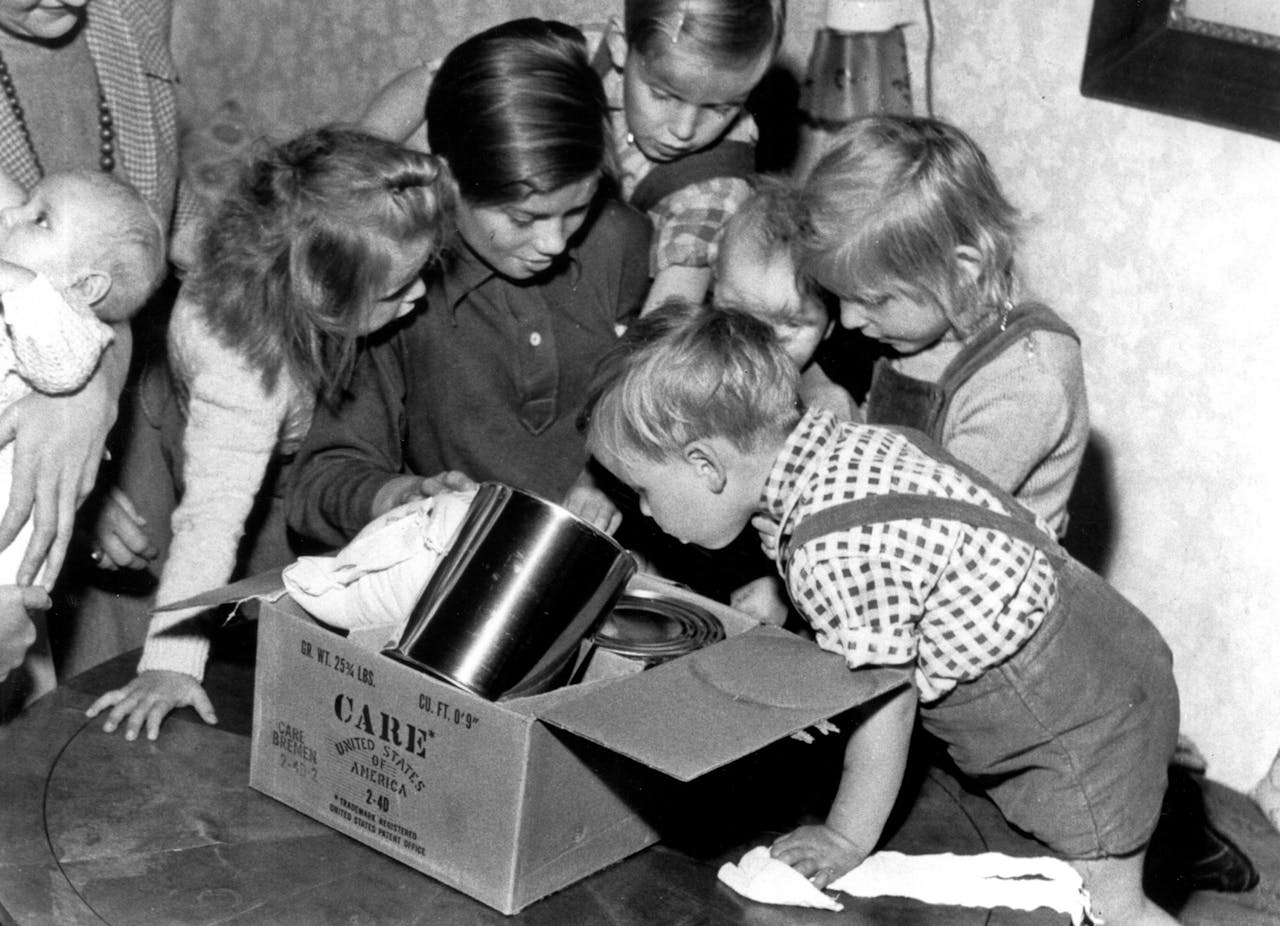 Historische zwart-witfoto: een groep kinderen opent een CARE-pakket