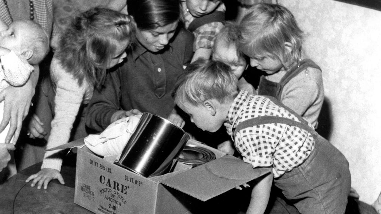 Historische zwart-witfoto: een groep kinderen opent een CARE-pakket