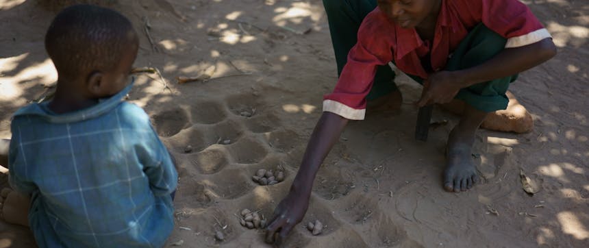 Twee kinderen spelen een traditioneel spel met pitten en kuiltjes in de grond