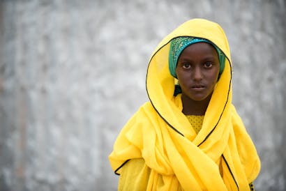 Een jonge vrouw in een fel geel gewaad kijkt in de camera