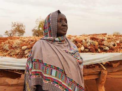 Aker Kiir Machar, 65 jr, uit Zuid-Soedan met haar oogst op de achtergrond