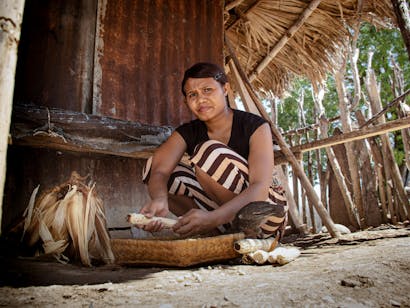 Een Indonesische vrouw zit voor haar huis eten klaar te maken