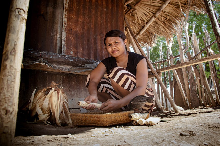 Een Indonesische vrouw zit voor haar huis eten klaar te maken